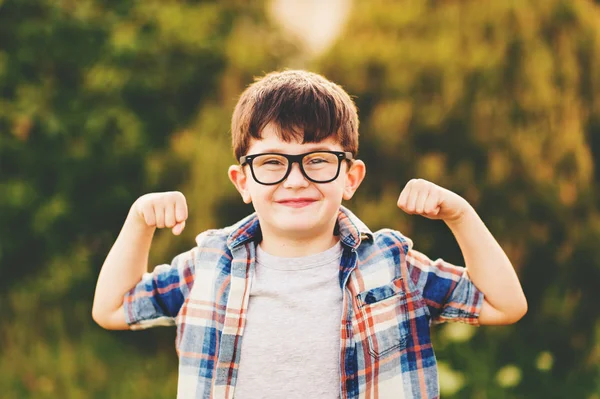 Menino forte e inteligente com expressão facial engraçada brincando ao ar livre, vestindo óculos e camisa xadrez azul — Fotografia de Stock