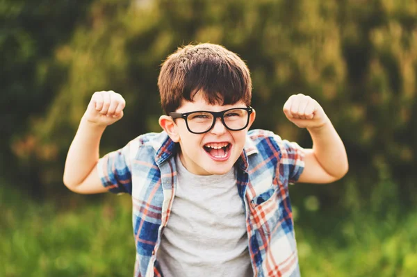 Starker und intelligenter kleiner Junge mit lustigem Gesichtsausdruck, der draußen spielt, Brille und blaues kariertes Hemd trägt — Stockfoto