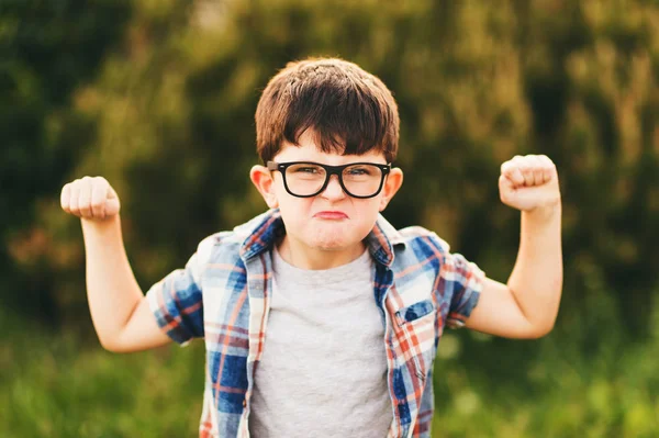 Menino forte e inteligente com expressão facial engraçada brincando ao ar livre, vestindo óculos e camisa xadrez azul — Fotografia de Stock