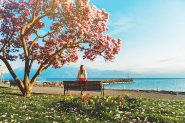 Lake Geneva, İsviçre şaşırtıcı manzaranın genç sarışın bir kadın. Çiçeği Manolya ağacının altında bankta oturan kadın