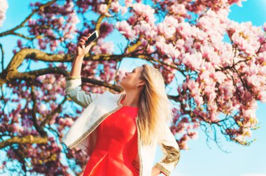 Genç güzel sarışın kadın taling selfie çiçek açan Manolya ağacı karşı