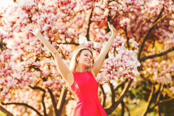Schöne, glückliche junge Frau genießt warmen, sonnigen Tag im Frühlingsgarten, trägt leuchtend rotes Kleid, Arme weit aufgerissen — Stockfoto