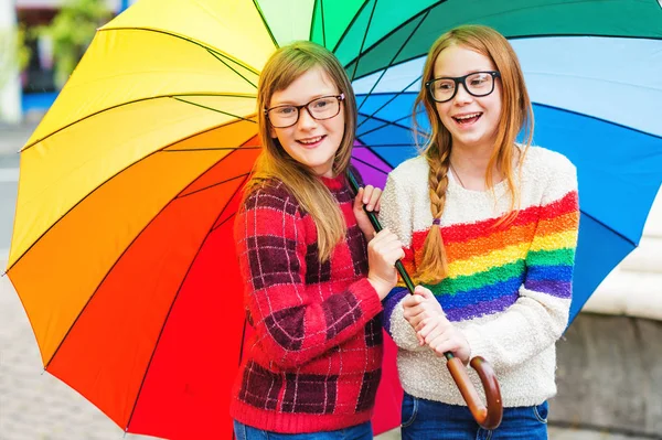 Grupo de duas meninas bonitos brincando fora sob grande guarda-chuva colorido, vestindo óculos e pulôveres quentes — Fotografia de Stock