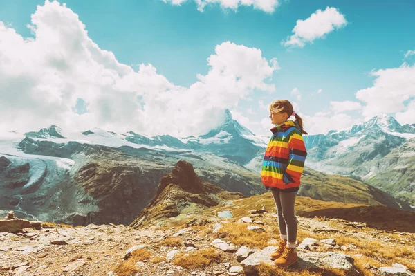 Menina bonito vestindo casaco colorido arco-íris brilhante e botas bege, descansando nas montanhas, Suíça, imagem do vintage — Fotografia de Stock