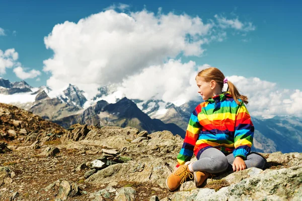 Menina bonito vestindo casaco colorido arco-íris brilhante, segurando bandeira suíça, de pé na frente da geleira Gornergrat, Suíça — Fotografia de Stock