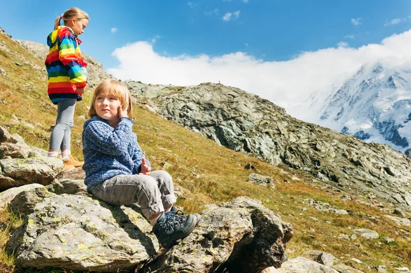 Anak-anak kecil yang lucu beristirahat di Gornergrat glacier, Swiss, Dua anak kecil bermain bersama di pegunungan, anak kecil dan kakak perempuannya mendaki di Alpen swiss, mengenakan pakaian berwarna-warni — Stok Foto