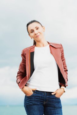 Kahverengi deri ceket giyen göl kenarında oturan güzel esmer kadın