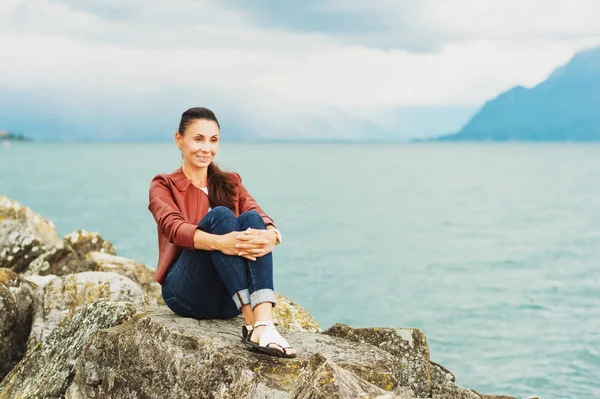 Mulher morena bonita descansando junto ao lago, vestindo jaqueta de couro marrom — Fotografia de Stock