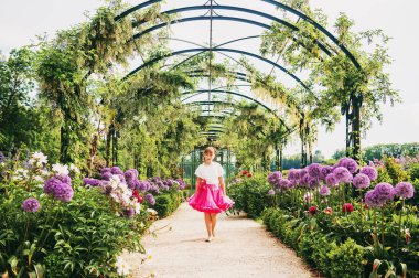 Adorable little girl playing in a beautiful flower garden on a nice sunny day, wearing white blouse and bright pink tutu skirt. Alley with giant allium giganteum flowers clipart