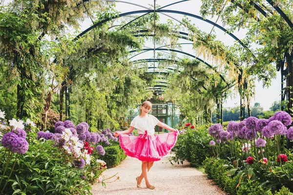 Urocza dziewczynka gra w piękny ogród kwiatowy w piękny słoneczny dzień, na sobie białą bluzkę i spódnicę jasne różowe tutu. Aleja z olbrzymie allium giganteum kwiaty — Zdjęcie stockowe
