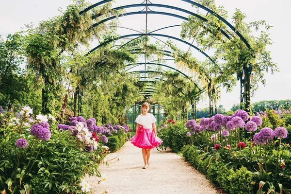 Bedårande liten flicka spelar i en vacker blomsterträdgård på en fin solig dag, klädd i vit blus och ljusa rosa tutu kjol. Gränd med giant allium giganteum blommor — Stockfoto