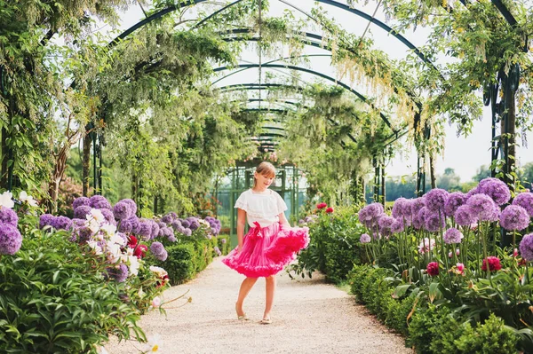 Bedårande liten flicka spelar i en vacker blomsterträdgård på en fin solig dag, klädd i vit blus och ljusa rosa tutu kjol. Gränd med giant allium giganteum blommor — Stockfoto