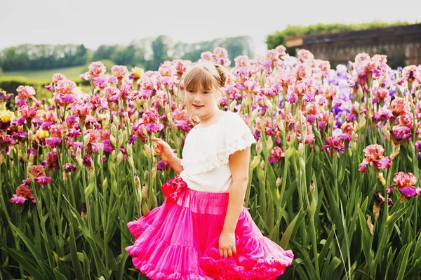 Carina bambina che gioca nel giardino fiorito di Iris in una bella giornata estiva, indossando camicia bianca e gonna tutù rosa brillante — Foto Stock