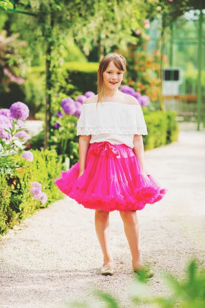 Ganska lite 9-10 år gammal flicka spelar i vacker trädgård, klädd i ljusa rosa tutu kjol — Stockfoto