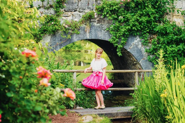 Douce petite fille jouant dans un petit jardin secret par une belle journée d'été, portant une jupe tutu rose — Photo