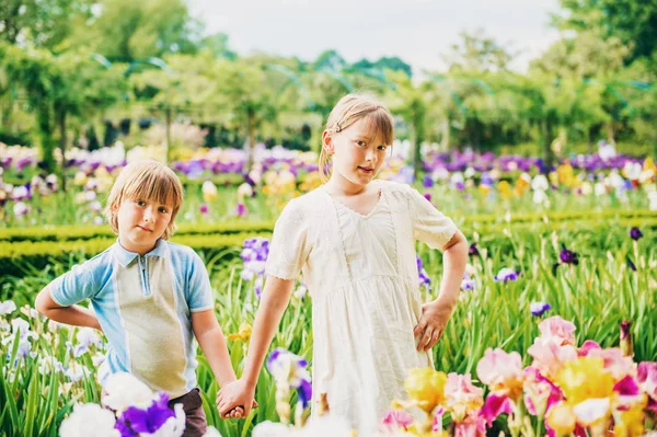 Group of two kids, little boy and girl, posing in beautiful english style garden, wearing retro style clothing, holding hands. Brother and sister playing together in amazing summer park Stock Image