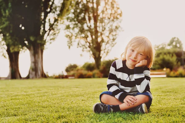 Открытый портрет очаровательного мальчика, сидящего на траве на закате — стоковое фото