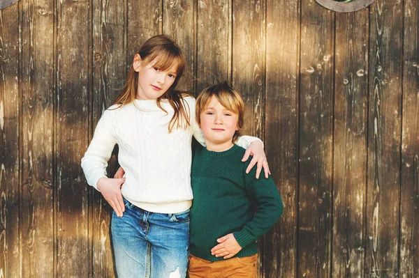 Outdoor Portret van twee schattige kinderen, broer en zus, het dragen van witte en groene truien, permanent tegen houten achtergrond — Stockfoto