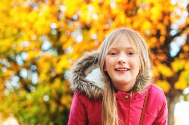 Açık yakın çekim portre sevimli 9-10 yıl eski küçük kız giyiyor sıcak kış ceket hood ve poz karşı sonbahar ağaç faux kürk ile