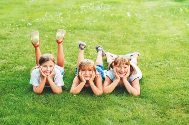 Grup kameraya seyir taze yeşil çim üzerinde yalan üç mutlu çocuk
