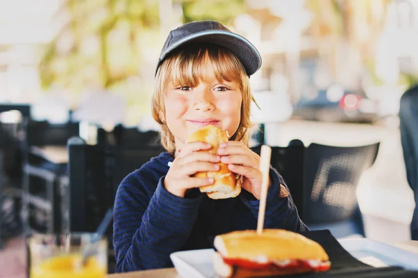 Cute little boy eating sandwich for breakfast at a seaside beach restaurant — Stock Photo, Image