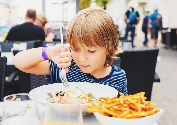 Little boy having lunch in the restaurant, child eating fresh salmon salad and french fries — Stock Photo, Image