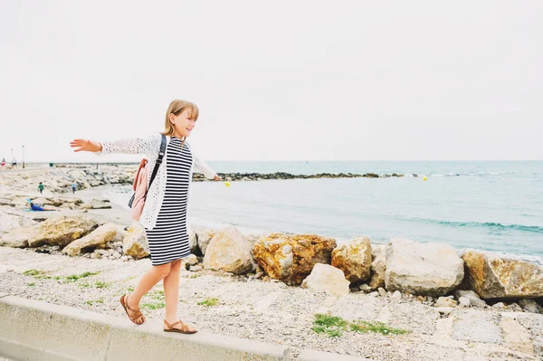 Şerit deniz elbise ve sırt çantası takmış küçük kız deniz kenarında tatil yaz zevk. Saintes-Maries-de-la-Mer, Camargue, Güney Fransa'nın başkenti alınan görüntü — Stok fotoğraf