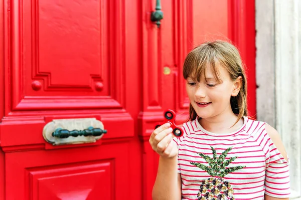 Menina da escola bonito jogando com fidget spinner vermelho. Brinquedo popular para aliviar o estresse para crianças e adultos da escola — Fotografia de Stock