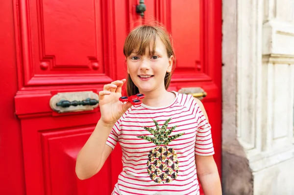 Sevimli okul kız kırmızı topluca spinner ile oynarken. Okul çocuklar ve yetişkinler için popüler bir stres giderici oyuncak