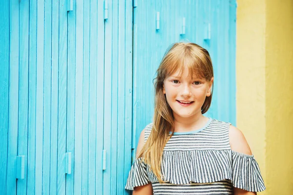 Retrato al aire libre de una linda niña preadolescente de 10 años con una camiseta de hombros fríos, posando contra persianas de madera azules — Foto de Stock