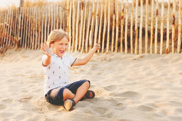 Komik çocuk çocuk deniz kum plajı üzerinde günbatımında dinleniyor. Genç çocuk zevk yaz tatil üzerinde Güney Fransa, giyen polo, kot şort ve Sandalet Ayakkabı — Stok fotoğraf