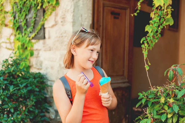 Cute little girl eating blue ice cream outdoors, wearing orange shirt and backpack, travel with kids — Stock Photo, Image