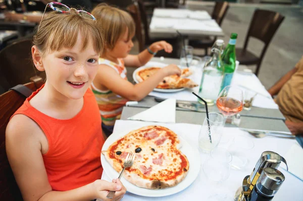 Happy little girl eating kid's pizza in the restaurant. Menu for children, heart shaped italian pizza — Stock Photo, Image