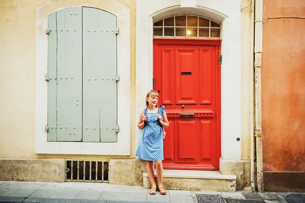 Dość mały turysta dziewczyna na ulicach Prowansji, noszenie niebieski wzór sukienka, Okulary przeciwsłoneczne i plecak. Podróż z dziećmi koncepcja. Zdjęcie zrobione w Arles, Francja — Zdjęcie stockowe