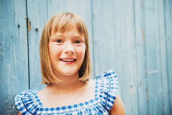 Närbild porträtt av bedårande kid flicka iklädd blå gingham klänning, poserar mot trävägg — Stockfoto