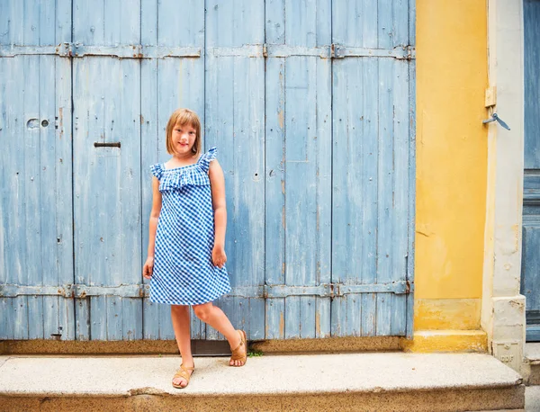 Ritratto all'aperto di adorabile bambina preadolescente che indossa un abito estivo blu di gingham, in posa contro la vecchia porta di legno — Foto Stock