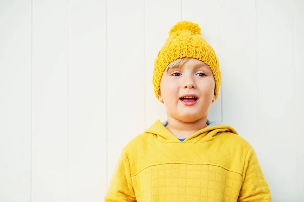 Outdoor close up portrait of cute little 5 year old boy wearing yellow knitted hat and sweatshirt with hood — Stock Photo, Image