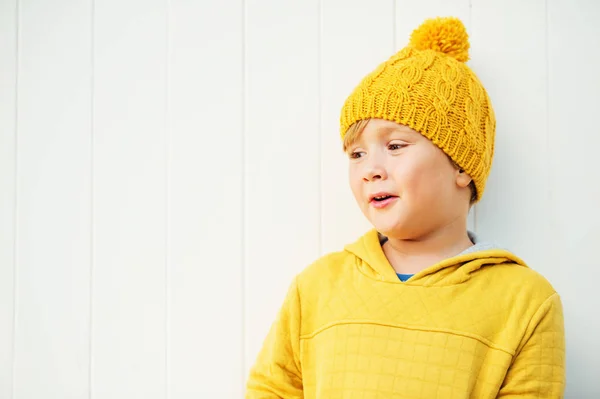 Outdoor close up portrait of cute little 5 year old boy wearing yellow knitted hat and sweatshirt with hood — Stock Photo, Image