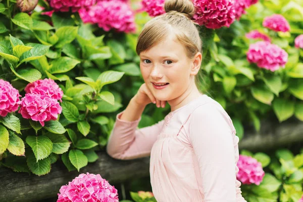 Retrato al aire libre de niña bonita jugando con hermosas flores de hortensias en el jardín de verano, con vestido de estilo bailarina, moño de pelo —  Fotos de Stock