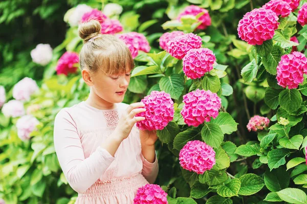 Ritratto all'aperto di graziosa bambina che gioca con bellissimi fiori di ortensia nel giardino estivo, indossando un abito in stile ballerina, un panino per capelli — Foto Stock