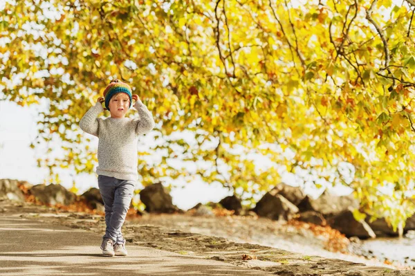 Ragazzino che gioca al lago in una giornata di sole, con cappello caldo, pullover grigio lavorato a maglia, pantaloni e scarpe — Foto Stock