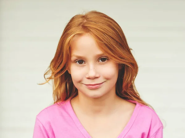 Retrato al aire libre de la linda niña de 8-9 años con el pelo largo y rojo, con chaqueta rosa, de pie sobre fondo blanco —  Fotos de Stock