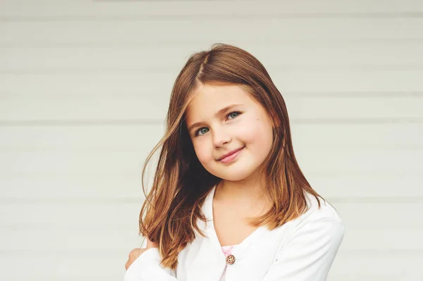 Außenporträt des süßen kleinen 8-9 jährigen Mädchens mit braunen Haaren, das weiße Jacke trägt und vor weißem Hintergrund steht — Stockfoto