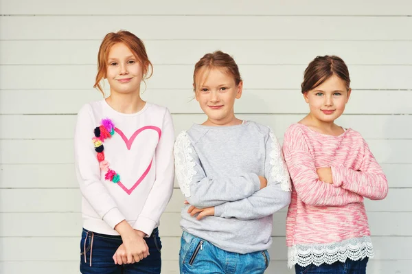 Groep van 3 kleine meisjes permanent buiten tegen witte houten achtergrond, het dragen van denim jeans en sweatshirts — Stockfoto