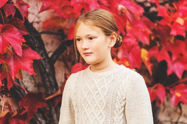 Autumn portrait of pretty little girl wearing knitted beige pullover dress, posing against wall with red ivy leaves — Stock Photo, Image