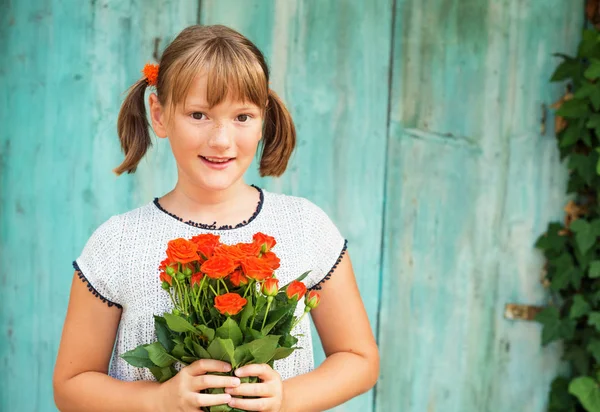 Outdoor portrait of a yong little girl of 9 years old, wearing white dress, holding fresh bouquet of beautiful orange roses — Stock Photo, Image