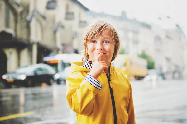Menino bonito brincando sob a chuva em uma cidade, vestindo capa amarela brilhante com capuz. Fotografias tiradas na Praça Saint-François, Lausanne, Suíça — Fotografia de Stock