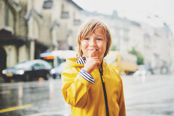 Cute little boy playing under the rain in a city, wearing bright yellow raincoat with hood. Image taken in Saint-Francois square, Lausanne, Switzerland