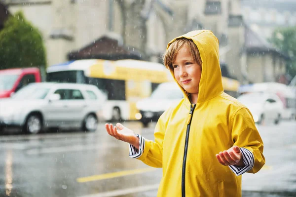 Cute little boy playing under the rain in a city, wearing bright yellow raincoat with hood. Image taken in Saint-Francois square, Lausanne, Switzerland — Stock Photo, Image