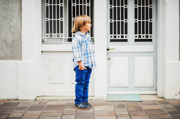 Retrato de moda al aire libre de lindo niño de 6 años con camisa y pantalones casuales a cuadros azules, manos en bolsillos — Foto de Stock